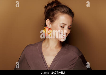 Hallo Herbst. Porträt der glückliche junge Frau im Bademantel mit Herbst Blatt Ohrring auf beigen Hintergrund isoliert. Stockfoto