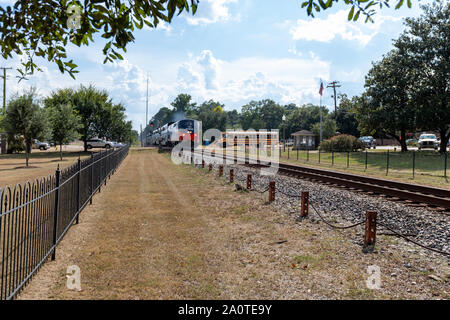 Magnolia, MS-USA, 17. September 2019: Amtrak Zug durch Magnolia, MS, an einem Verkehr Kreuzung mit Schulbus, in der kleinen Stadt USA. Stockfoto