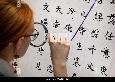 Eine Frau schaut durch ein Vergrößerungsglas an chinesischen Zeichen an der Ausstellung "Große Chinesische Kalligraphie und Malerei" bei Sokolniki exhibition cent Stockfoto