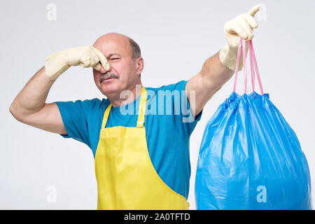 Hispanic reife männliche schließen seine Nase und einem stinkenden Abfallbeutel auf weißem Hintergrund. Umweltverschmutzung Konzept. Studio shot Stockfoto