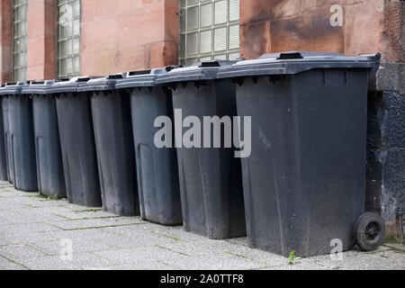 Schwarz wheelie Bins in einer Zeile auf Straßen mit Hausnummern auf der Vorderseite gedruckt Warten bin Männer zu sammeln Stockfoto