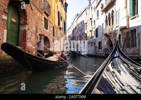 Ein gondoliere in einem traditionellen gestreiftes Hemd und Stroh Kreissäge Hut auf einer Gondel auf den Kanälen von Venedig, Italien. Tragen moderne Spiegel Sonnenbrille. Stockfoto