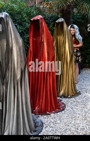 "Hüter der Zeit" Skulptur von Manfred Kielnhofer, Venedig, Italien, 2019. Ein stehendes Mädchen im Einklang mit ihren Mantel über den Kopf imitiert die Statuen Stockfoto