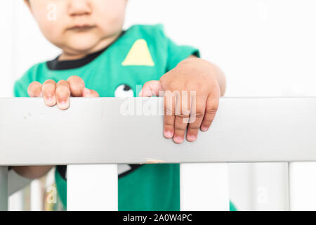 In der Nähe von Babys Hände während des Aufstehens und halten auf dem Geländer der Krippe. Das Tragen eines niedlichen grünen T-Shirt in einem hellen minimalistischen modernen nurs Stockfoto