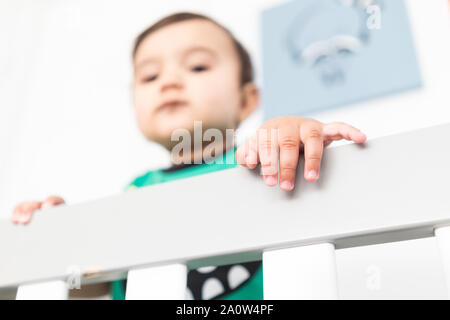 In der Nähe von Babys Hände während des Aufstehens und halten auf dem Geländer der Krippe. Das Tragen eines niedlichen grünen T-Shirt in einem hellen minimalistischen modernen nurs Stockfoto