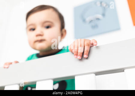 In der Nähe von Babys Hände während des Aufstehens und halten auf dem Geländer der Krippe. Das Tragen eines niedlichen grünen T-Shirt in einem hellen minimalistischen modernen nurs Stockfoto