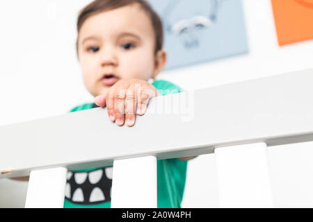 In der Nähe von Babys Hände während des Aufstehens und halten auf dem Geländer der Krippe. Das Tragen eines niedlichen grünen T-Shirt in einem hellen minimalistischen modernen nurs Stockfoto