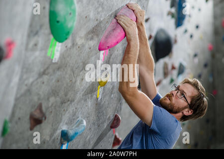 Starke gesunde aktive stattlicher Mann mit Bart tragen modische Brille Klettern an der Wand mit Farbe hält während des Trainings Workout Stockfoto