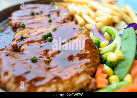 In der Nähe von Essen vom Grill Fleisch, Rindfleisch Steak mit schwarzem Pfeffer Soße auf einer heissen Platte gekrönt, Abendessen mit Salat und Pommes frites Stockfoto