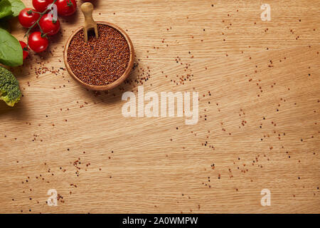 Blick von oben auf die Rote Quinoa Samen in Houten in der Nähe von roten Tomaten, Brokkoli und Spinat Blätter auf hölzernen Tisch Stockfoto