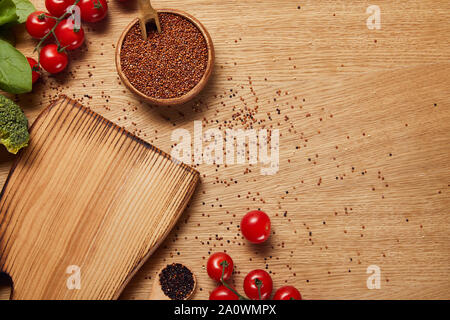 Blick von oben auf die Rote Quinoa Samen in Houten in der Nähe von Schneidebrett und rote Tomaten Stockfoto