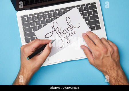 Sicht des Menschen Schreiben auf Karte mit vielen Dank Schriftzug in der Nähe von Laptop auf blauem Hintergrund 7/8 Stockfoto
