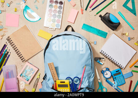 Blick von oben auf die verschiedenen Schulmaterial mit blauer Rucksack auf hölzernen Schreibtisch Stockfoto