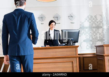 Rückansicht des Kaufmanns in der Nähe von fröhlichen Empfang im Computer Monitor suchen Stockfoto