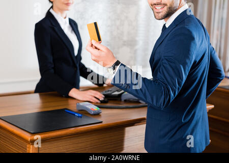 7/8-Ansicht von fröhlichen Geschäftsmann holding Kreditkarte in der Nähe Rezeption Stockfoto