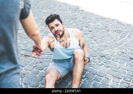 7/8 Schuß von Frau helfen verletzten Sportler sitzen auf Pflaster Stockfoto
