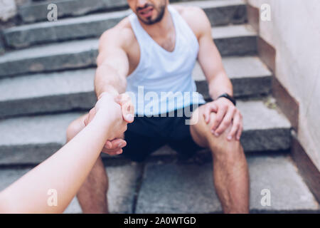 7/8 Schoß der Frau die Hand zu geben, verletzte Sportler sitzen auf der Treppe und leiden unter Schmerzen Stockfoto