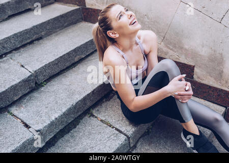 Verletzte Sportlerin, die beim Sitzen auf der Treppe und leiden unter Schmerzen im Bein Stockfoto