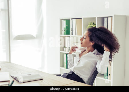 Ziemlich afrikanische amerikanische Geschäftsfrau weg schauen beim Sitzen am Arbeitsplatz und leiden unter Hitze im Büro Stockfoto