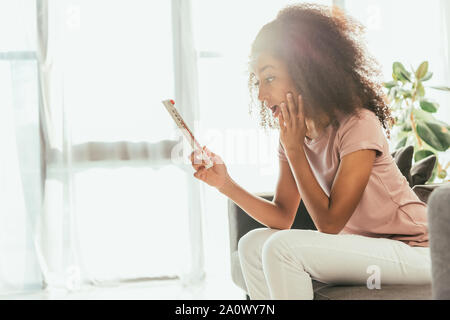 Afrikanische amerikanische Frau auf der Suche nach Thermometer, während von der Sommerhitze zu Hause leiden schockiert Stockfoto