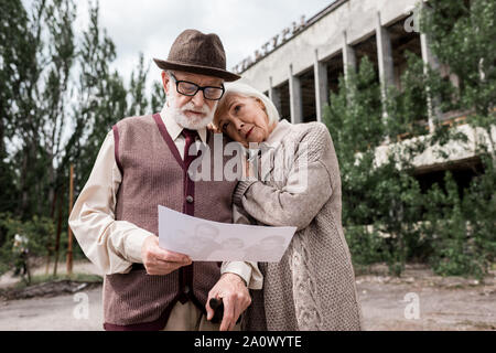 PRIPYAT, UKRAINE - 15. AUGUST 2019: ältere Paare bei Foto in der Nähe von Gebäude suchen in Tschernobyl. Stockfoto