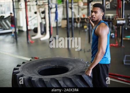 Portrait von Stattlichen muskulösen Mann an der Kamera stehend, durch schweren Reifen während Cross Training im modernen Fitnessraum, Kopie Raum Stockfoto