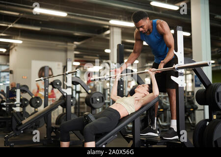 Portrait der afroamerikanischen Fitness Coach helfen jungen Frau anhebende Gewichte auf der Werkbank in einen modernen Fitnessraum, kopieren Raum Stockfoto