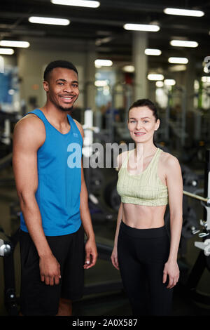 Portrait des jungen Paares lächelnd an Kamera und posiert im modernen Fitnessstudio, Fitness Trainer Konzept Stockfoto
