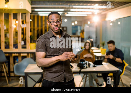 Angesichts der stattlichen African Business Mann, holding Tablet auf dem Hintergrund der Völker gemischtrassiges Team Meeting, im Büro. Stockfoto