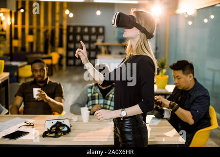 Frau in schwarzer Kleidung tragen VR-Brillen durch ihre multiethnical Kollegen in modernen Büro beobachtet Stockfoto
