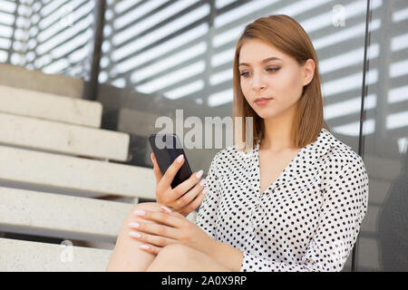 Portrait schöne junge geschäftsfrau Textnachrichten auf Ihrem Smartphone. Mädchen sitzen im Freien in der Nähe von Ihrem Büro oder Hochschule in formale Abnutzung mit langen Bob haircu Stockfoto