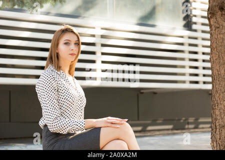 Junge Mode Frau draußen sitzen. Mädchen sitzen im Freien in der Nähe von Ihrem Büro oder Hochschule auf grünem Rasen Campus in formale Abnutzung mit langen Bob haircu Stockfoto