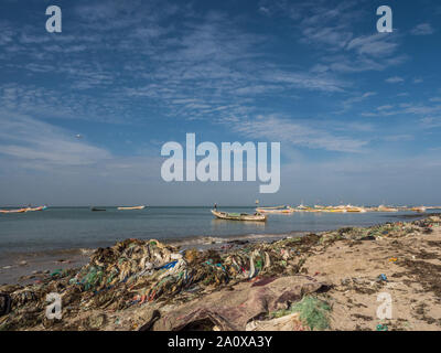 Senegal, Afrika - Januar 26, 2019: Viel Plastiktüten am Ufer des Ozeans. Umweltverschmutzung Konzept. Bunte Fischerboote im Hintergrund. Senegal. Stockfoto