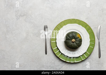 Halloween Tisch auf grauem Hintergrund mit Messer und Gabel. Konzept der Abendessen's Thanksgiving Tabelle einrichten. Minimale Servierteller mit grünem Kürbis. Top Stockfoto