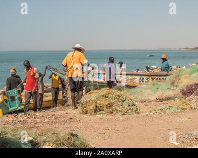 Nianing, Senegal - Januar 2, 2019: Fischer sammeln Fisch aus farbigen Holz Fischerboot am Strand. Afrika Stockfoto