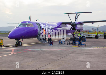 21. September 2019 eine FlyBe Dash 8 Verkehrsflugzeug mit Gepäck und Passagiere Handler auf dem Vorfeld des George Best City Airport in Belfast, Nordirland Stockfoto