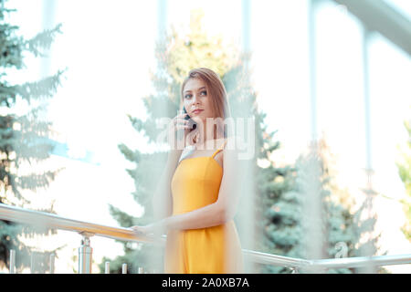 Telefon sprechen. Portrait von attraktiven jungen Frau in casual gelben Kleid Tagträumen auf der Seite außerhalb sprechen über das Telefon in der Nähe Ihres Büros, Bild Stockfoto