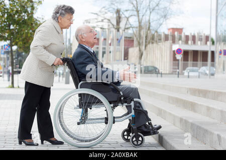 Rollstuhlfahrer und Frau vor der Treppe Barriere Stockfoto