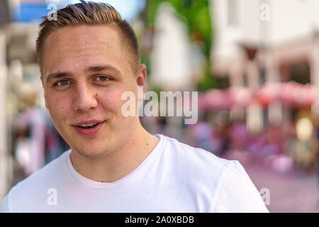 Lächelnd freundlich heiter attraktiven jungen Mann zu Fuß in einer städtischen Straße in einer Nahaufnahme Kopf und Schultern portrait Stockfoto