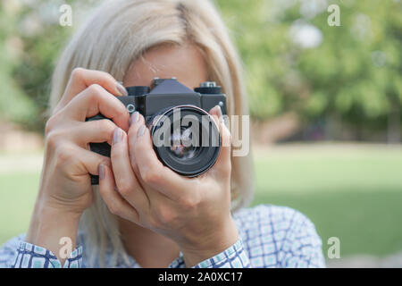 Mädchen, blond mit einer Kamera konzentriert sich im Park. Vor dem Hintergrund der grünen Gras und Bäumen. Bild für den Fotografen Visitenkarte. Stockfoto