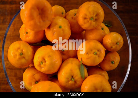 Frische Hausgewachsene gesunde Orangen Mandarinen in eine Glasschüssel auf hölzernen Tisch Stockfoto