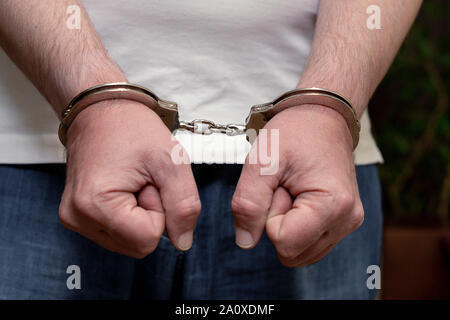 Männer die Hände in den Handschellen. Ein Mann in einem weißen T-Shirt in Handschellen. Close-up Stockfoto