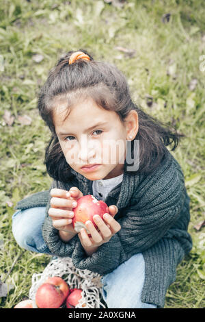 Süße Mädchen in einer grauen Jacke und Jeans frisst einen roten Apfel Stockfoto