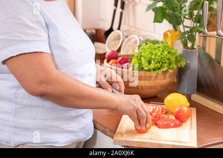 Geschlossen bis senior Hand schneiden Tomaten auf Holz Schneidebrett. Vorbereitung von Salat, gesunden Ruhestand lifestyle Konzept. Stockfoto