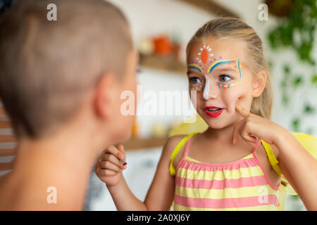 Junge Vorschüler Mädchen mit Gesicht Farbe an ihre Mutter. Halloween oder Karneval Familie Lebensstil Hintergrund. Schminken und Verkleiden. Stockfoto