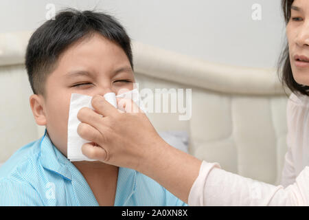 Sick asiatische Kind wischen oder Reinigung der Nase mit einem Taschentuch, während die Mutter ihm zu helfen. Health Care, Fieber und Grippe Konzept. Stockfoto