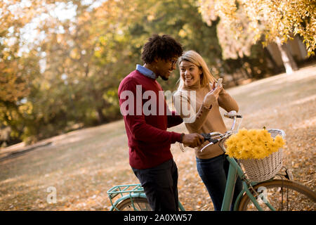 Multirassischen junges Paar mit dem Fahrrad stehen im Herbst Park und mit Handy Stockfoto