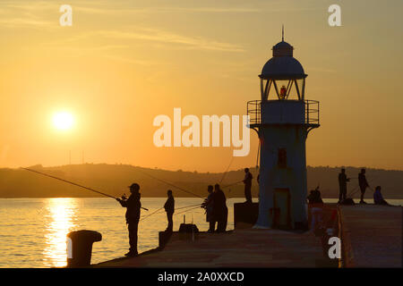 Angler neben dem Leuchtturm am Ende der Brixham Breakwater, wie die Sonne untergeht. Stockfoto