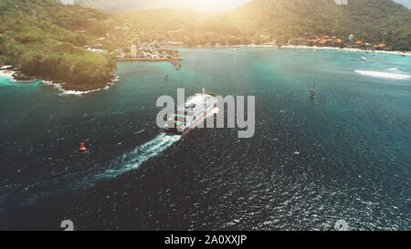 Luftaufnahme über Fähre segeln in Hafen. Reisen Urlaub Freizeit Paradies Tourismus. Sonnenuntergang Berg Hügel im Hintergrund. Schöne Natur Landschaft in tropischen Insel Bali. Filmische Filter Stockfoto