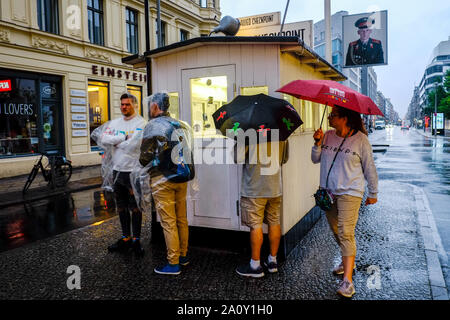 06 Juli 2019, Berlin: Am Abend sind Touristen im Regen stehen neben der Pförtnerloge am ehemaligen Grenzübergang Checkpoint Charlie in der Friedrichstraße. Foto: Stefan Jaitner/dpa Stockfoto